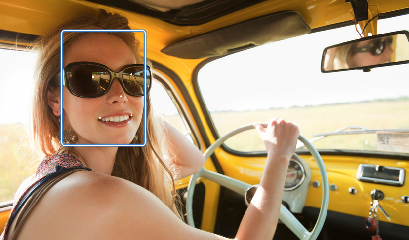 Mujer sonriente con gafas de sol que conduce un coche clásico amarillo en carretera abierta.