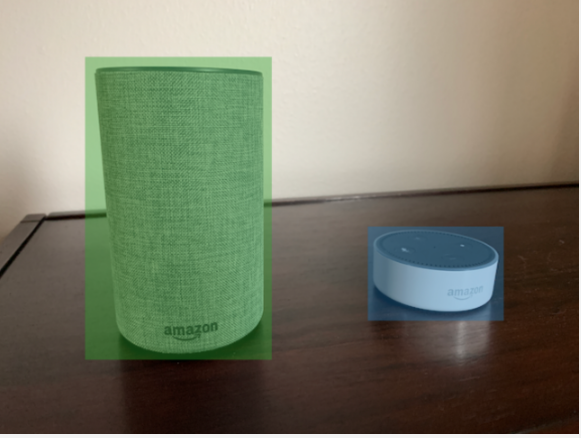 兩個 Amazon 智慧喇叭，一個帶有綠色週框方塊和一個藍色週框方塊，位於木頭表面。
