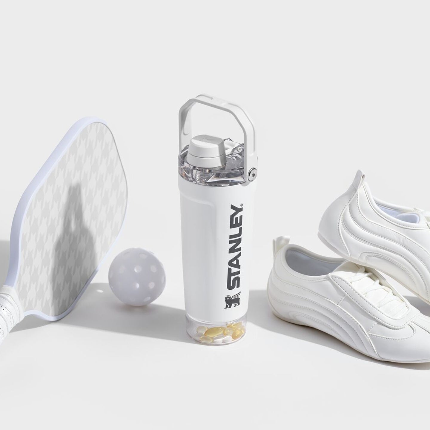 White Stanley 1913 water bottle with pill compartment base, beside a pickleball paddle, ball, and white sneakers.