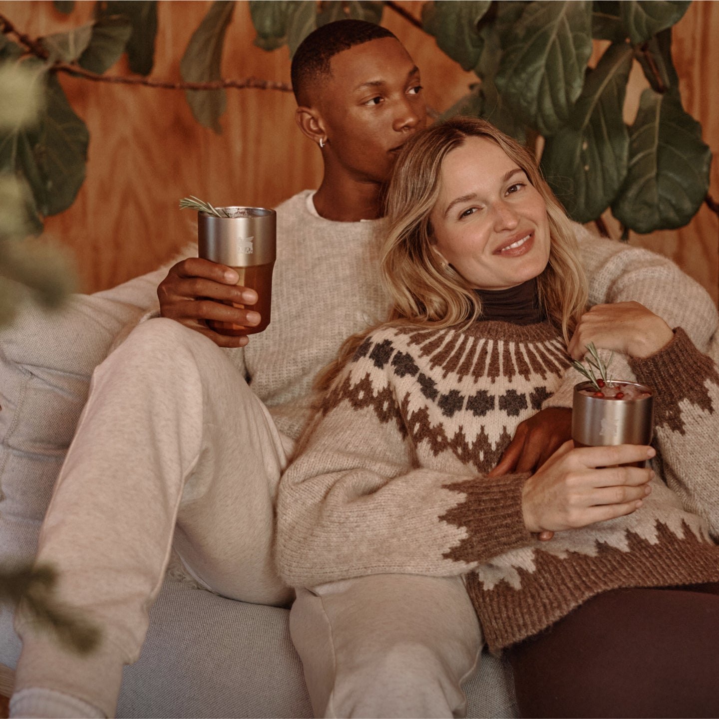 Two people relaxing together holding Stanley 1913 stainless steel tumblers with rosemary garnishes in a cozy autumn setting.