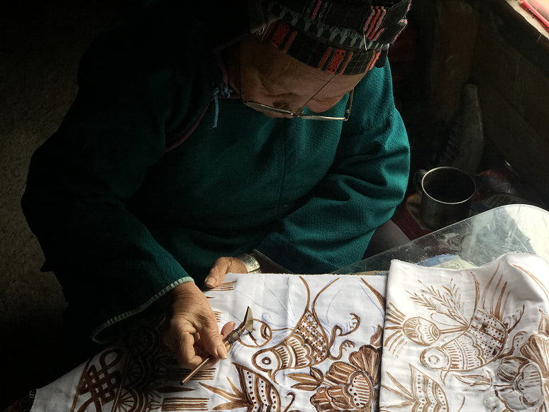 Artisan applying intricate batik patterns on white fabric using a traditional tjanting tool.