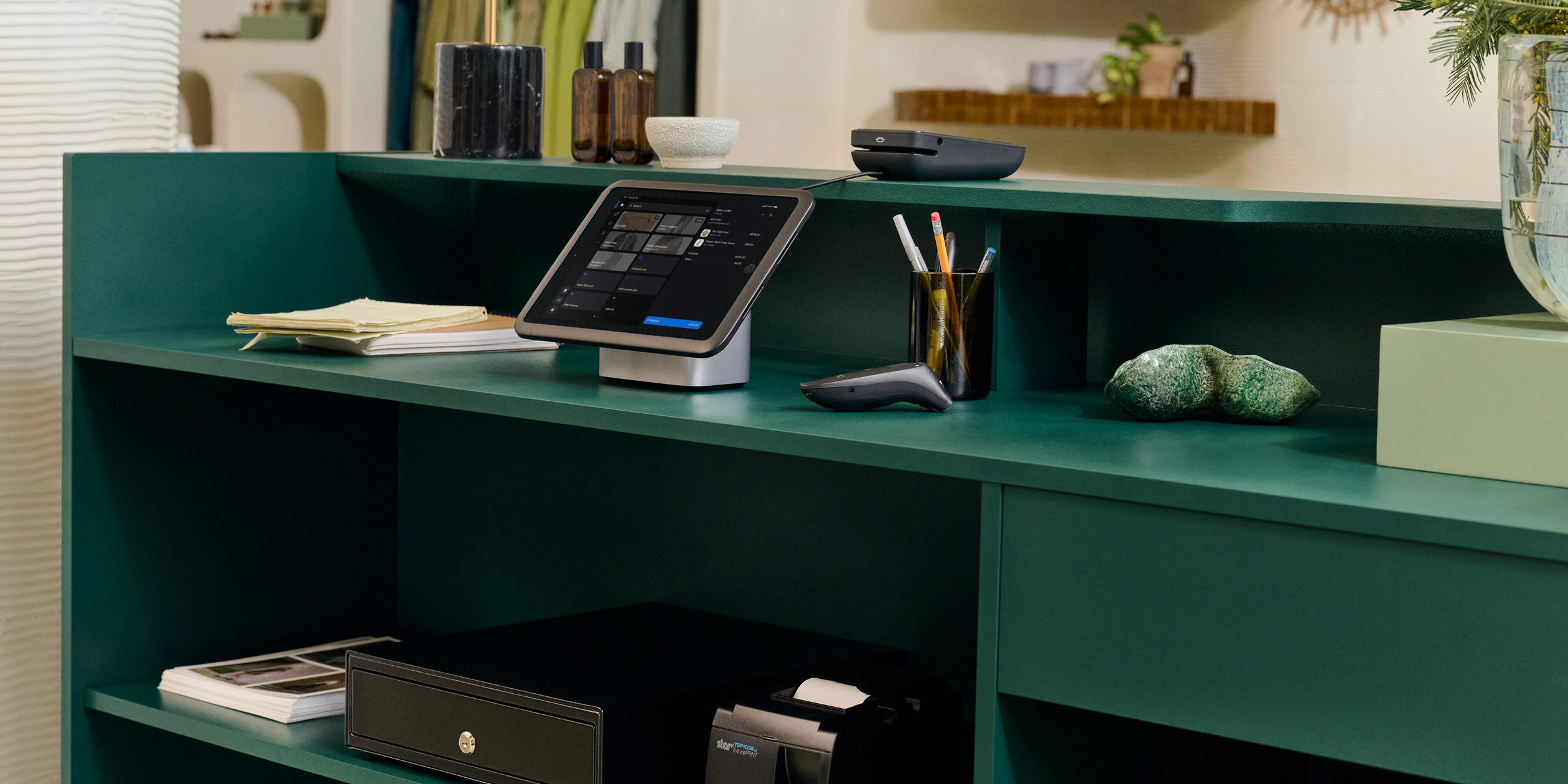 Behind the retail counter showcases a point of sale setup including the tablet stand, POS Terminal, cash drawer, and receipt printer.