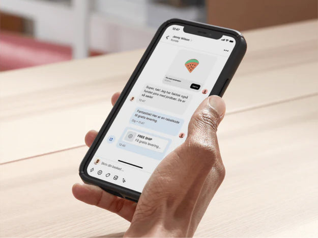 En virksomhedsejer sidder ved sit bord i baglokalet og bruger Shopify Inbox til at chatte med en kunde på sin mobilenhed. Hun deler en rabatkode i chatten for at lukke handlen.