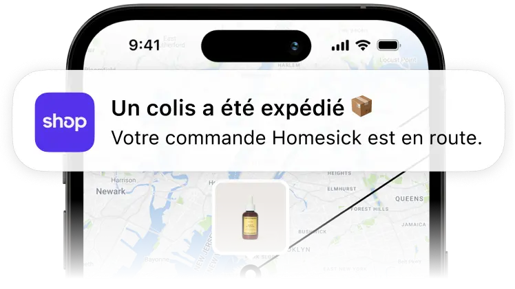 Un téléphone portable affichant une notification de l’application Shop qui indique qu’un colis provenant de Homesick a été expédié, avec une carte de suivi en arrière-plan