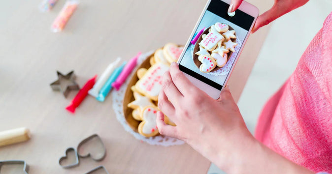 Seseorang sedang memfoto berbagai kue kering di atas meja dengan ponsel.