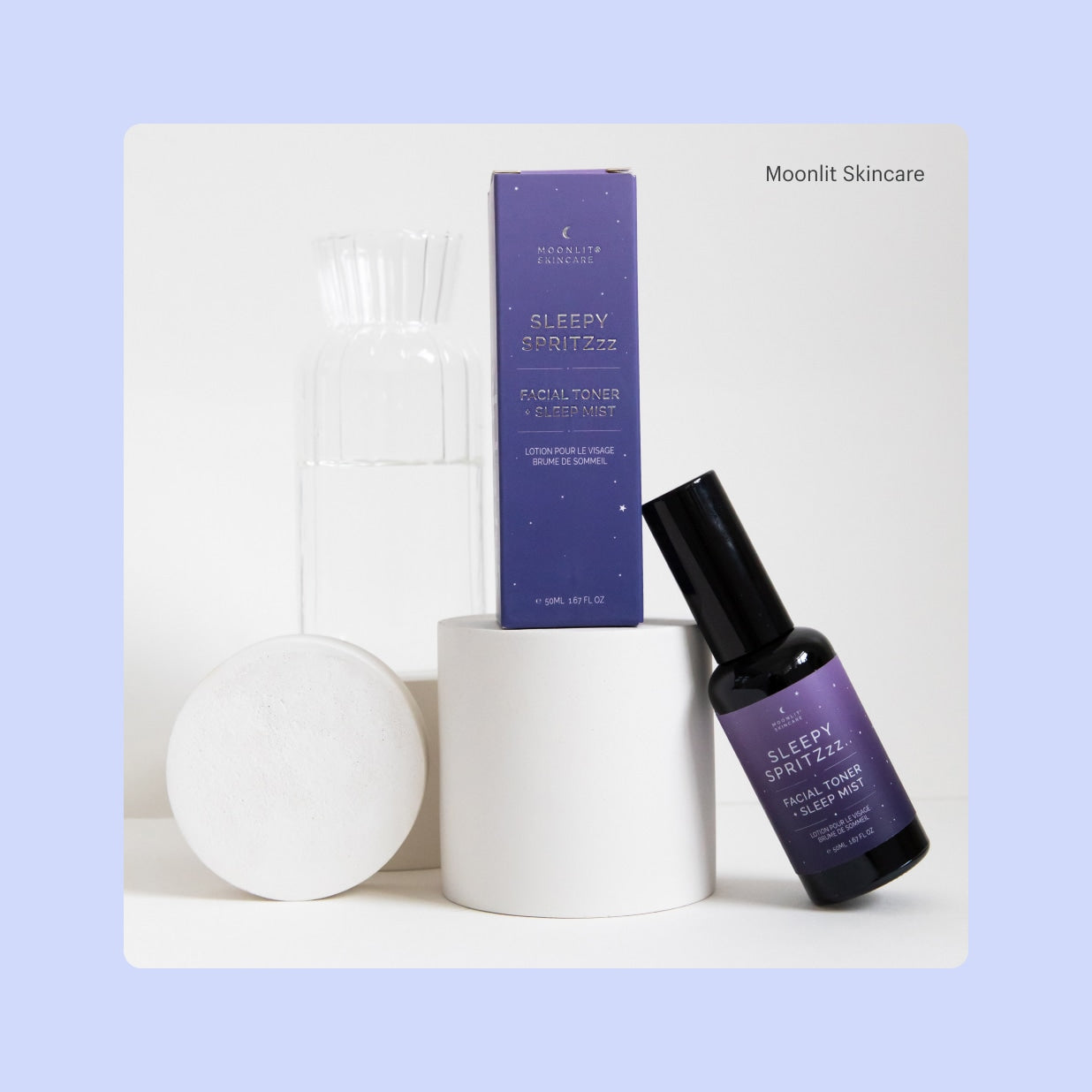 Ein Produkt-Display mit der lilafarbenen Verpackung des Gesichtswassers Sleepy Spritzzz von Moonlit Skincare und einer kleinen Sprühflasche des Gesichtswassers Sleepy Spritzzz.